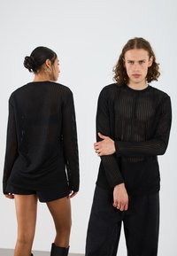 Black long-sleeve top featuring a grid texture and open knit design, paired with black shorts and dark wide-leg pants.