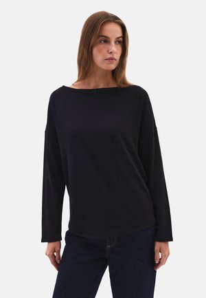 Schwarzes Langarmoberteil mit weitem U-Boot-Ausschnitt und abgesenkten Schultern, aus weichem Stoff; kombiniert mit dunklen Jeans, minimalistisches Design.