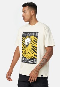 Cremefarvet t-shirt med korte ærmer, der har et grafisk motiv af en gul tegneseriekat på en sort og gul stribet baggrund med teksten "GARFIELD".