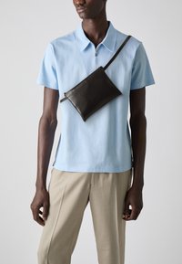 Lys blå kortermet zip-up polo skjorte med avslappet passform, kombinert med beige bukser og en mørk brun lær crossover veske.