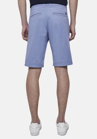 Pantaloni corti viola chiaro realizzati in un tessuto morbido, dotati di tasche posteriori e parte anteriore piatta. Indossati con sneaker bianche per un look casual.
