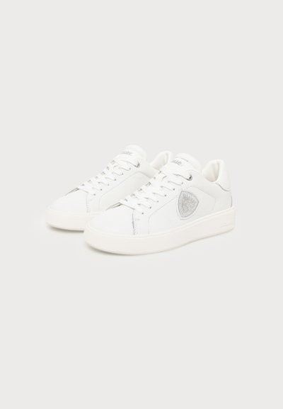 Pair of white low-top sneakers with laces and a silver shield emblem on the side, displayed on a plain light background.
