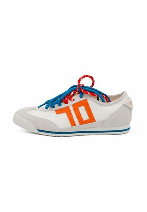 Zapatilla deportiva blanca de caña baja con detalles en beige, número 70 naranja en el lateral, cordones azules y rojos, y una franja azul en la suela blanca.