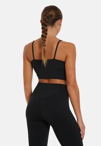 Čierny športový podprsenka a legíny s vysokým pásom vyrobené z elastického materiálu. Podprsenka má tenké ramienka a priliehavý strih, ktorý zvýrazňuje pás.