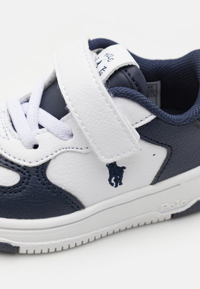Scarpa sportiva in sintetico bianco e blu navy con chiusura a strappo, superficie testurizzata e logo di un cavallo ricamato sul lato.
