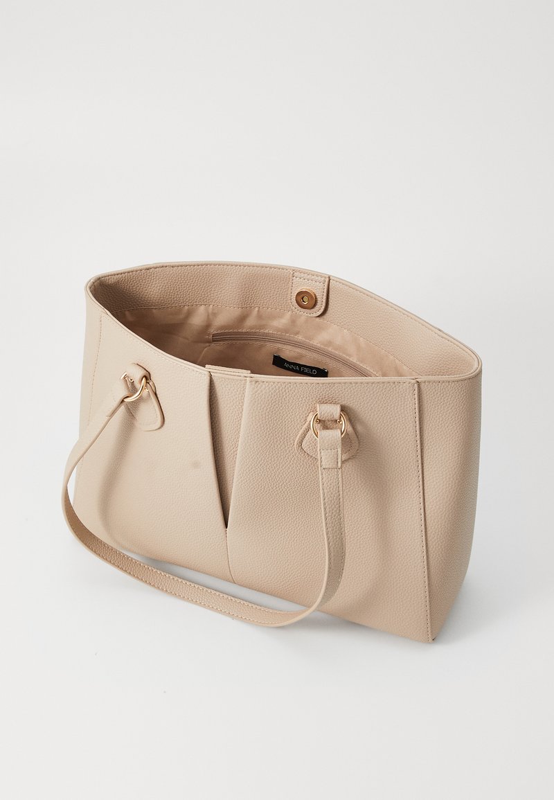 Bolso tote sintético beige con exterior texturizado, herrajes en tono dorado, dos asas y un interior espacioso que cuenta con un pequeño bolsillo con cremallera.