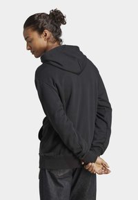 Sweat à capuche noir avec une poche kangourou, texture douce et capuche réglable avec cordon, associé à un jean en denim foncé. Vue de dos montrée.