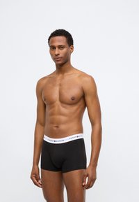 Boxer aderenti neri con un elastico bianco in vita che presenta il logo "Tommy Hilfiger". Il materiale sembra liscio e aderente.