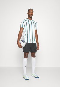 Nike sportkleding set met een wit shirt met groene en marineblauwe verticale strepen, zwarte shorts, witte sokken en kleurrijke sportschoenen.