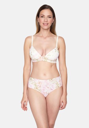 Woman wearing floral patterned bra and matching high-waist briefs, standing against a plain light gray background, smiling gently.