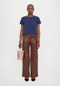 Σκούρο μπλε κοντομάνικο μπλουζάκι, καφέ ψηλόμεσα δερμάτινα παντελόνια με ζώνη, ροζ και πολύχρωμη τσάντα τύπου bucket, μαύρα μυτερά παπούτσια.