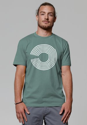 T-shirt en coton vert avec un motif de cercles concentriques blancs sur le devant. Col ras du cou, manches courtes et coupe décontractée.