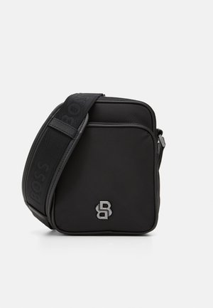 Bolsa transversal preta em tecido texturizado com fecho de zíper. Apresenta um accentuador de logotipo e uma alça ajustável estampada. Design compacto em forma de quadrado.