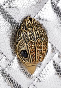 Metallisch zilveren textuur met een gouden decoratieve klem, voorzien van bladeren ontwerpen en bruine edelstenen. Zwarte accenten zorgen voor de afwerking.
