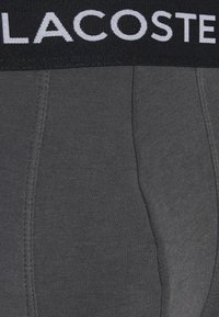 Caleçons boxers gris foncé avec une ceinture noire arborant le logo blanc "LACOSTE". Tissu doux et extensible avec texture côtelée et coutures plates.