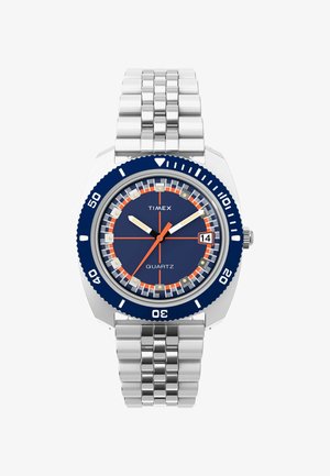 Hodinky Timex s quarčovým strojčekom, modrým ciferníkom, oranžovými a bielymi značkami, zobrazením dátumu na 3. hodine, strieborným kovovým remienkom a modrým otočným rámčekom.