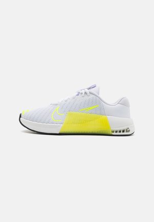 Chaussure de sport blanche avec tige en mesh, accents jaune néon sur la semelle intermédiaire et le logo, semelle extérieure noire, vue de côté.