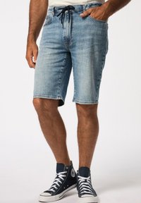 Shorts de mezclilla en azul claro, con cintura ajustable con cordón, bolsillos laterales y dobladillos enrollados, complementados con zapatillas altas en azul marino.
