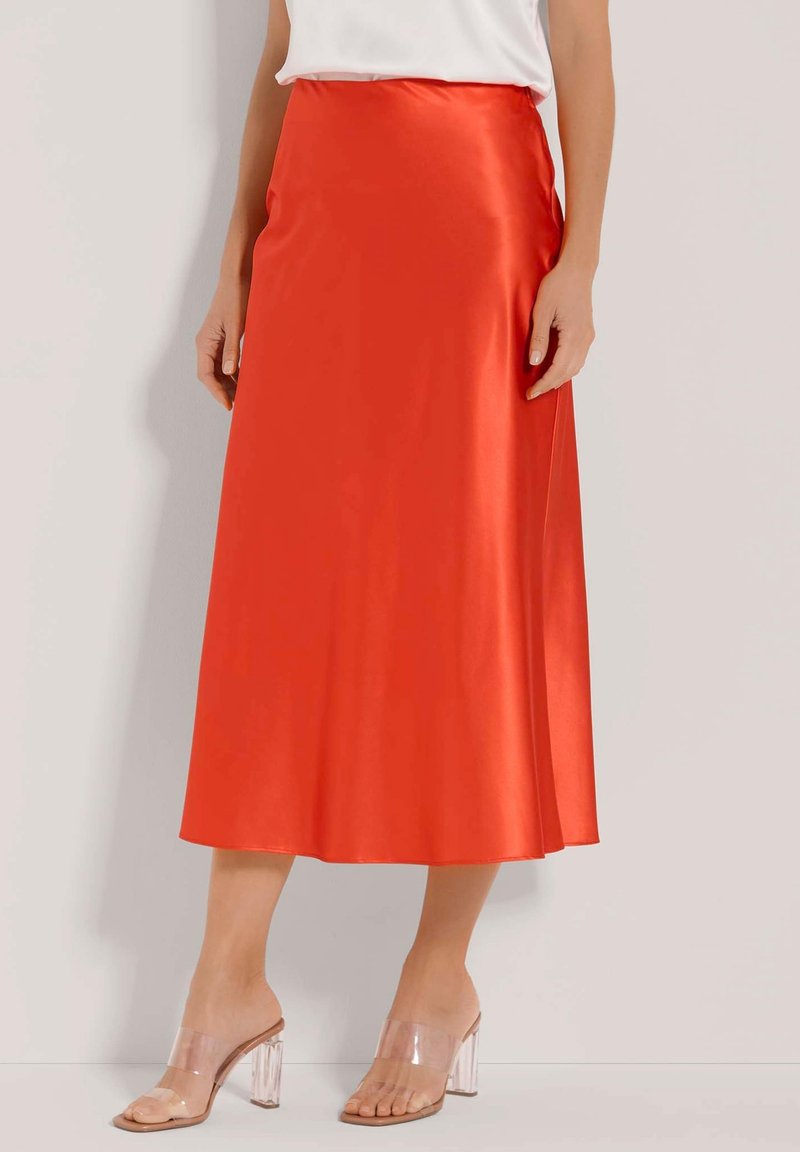 Satinorange Rock mit einem fließenden Design, knielangem Saum und glatter Textur. Kombiniert mit klaren Absatzsandalen.