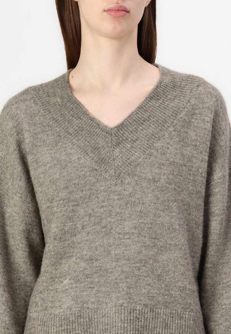 Pull en laine gris avec un col en V, des poignets côtelés et un ourlet. Texture douce, coupe décontractée et design minimaliste.