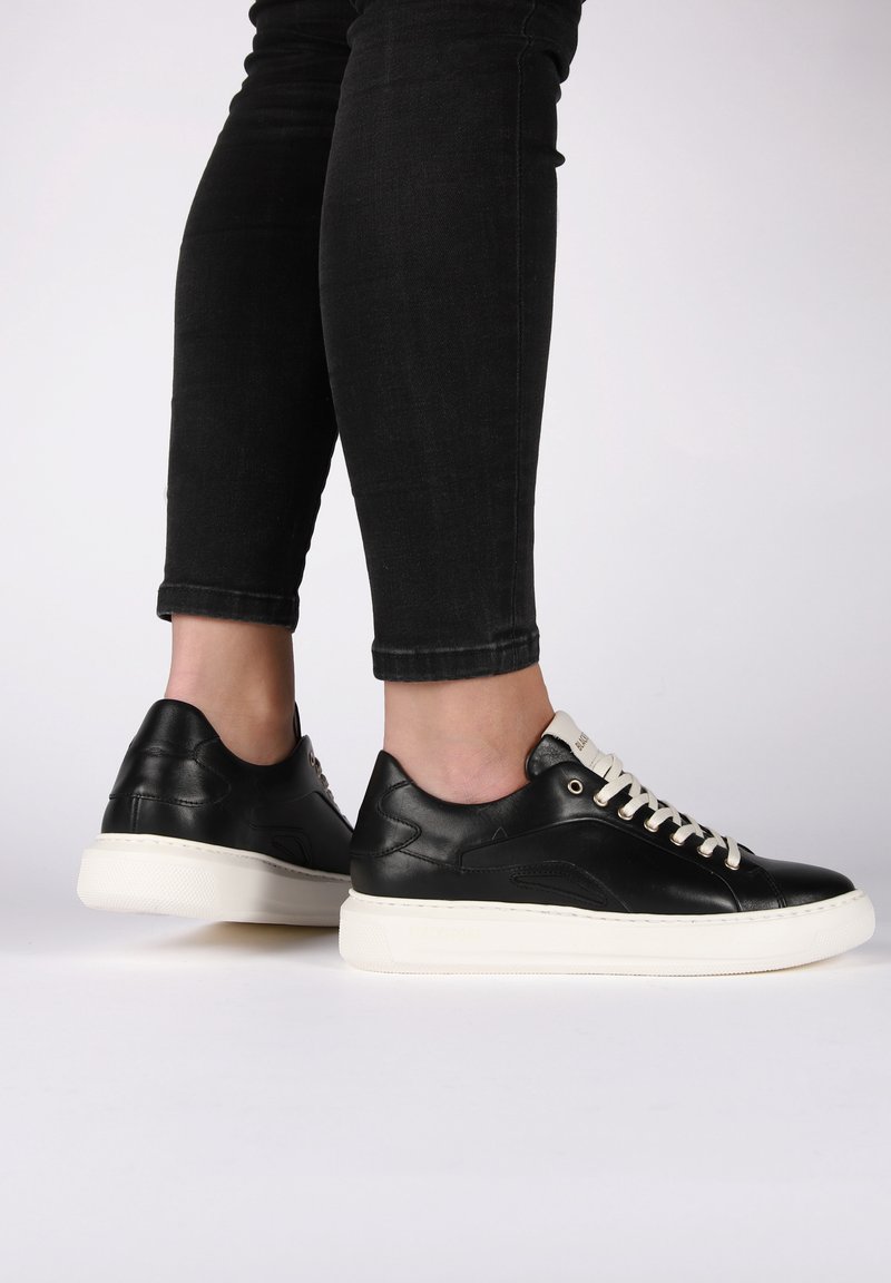 Černé kožené tenisky s bílou gumovou podrážkou, kulatým špičatým designem, krémovými tkaničkami a decentním bočním detailem. Vhodné pro volný čas.