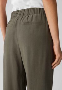 Pantalons larges kaki avec une taille élastique et deux poches arrière. La texture semble lisse et légère.