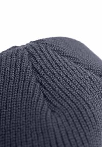 Berretto in maglia di colore grigio scuro con una texture a coste e sottili linee verticali, design con corona arrotondata. Materiale morbido ed elastico.