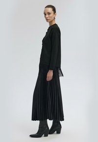 Musta pitkähihainen paita, jossa on fringed-tietoa, yhdistettyyn mustaan koko pitkään hameeseen. Viimeistelty mustilla korokepohjaisilla nilkkureilla.
