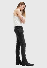Schwarze Jeans aus Denim mit schmalem Schnitt, ausgestattet mit einem klassischen Fünf-Taschen-Design und dezenten Steppdetails, kombiniert mit einem weißen ärmellosen Oberteil.