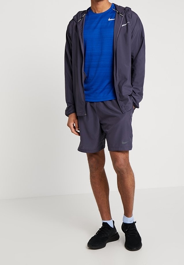 Men's activewear: navy blue moisture-wicking short-sleeve shirt, gray shorts with perforated design, lightweight jacket, black sneakers.