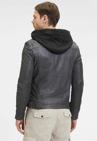 Giubbotto in pelle nera con dettagli trapuntati e cappuccio rimovibile, caratterizzato da una vestibilità aderente e sottili dettagli di texture.
