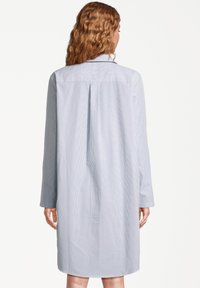 Jasnoniebieska sukienka koszulowa w paski, z długimi rękawami, kołnierzykiem i plisą z tyłu. Tkanina wydaje się gładka, ma nieco luźny krój i zaokrąglony dół.