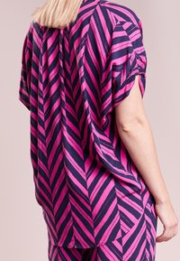 Top a maniche corte con un audace motivo a zigzag rosa e blu navy, caratterizzato da una vestibilità rilassata, tessuto morbido e un orlo arrotondato.