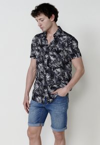 Camisa de manga corta en negro con un patrón de hojas blancas, combinada con pantalones cortos de mezclilla enrollados. La camisa cuenta con un diseño de botones y cuello.