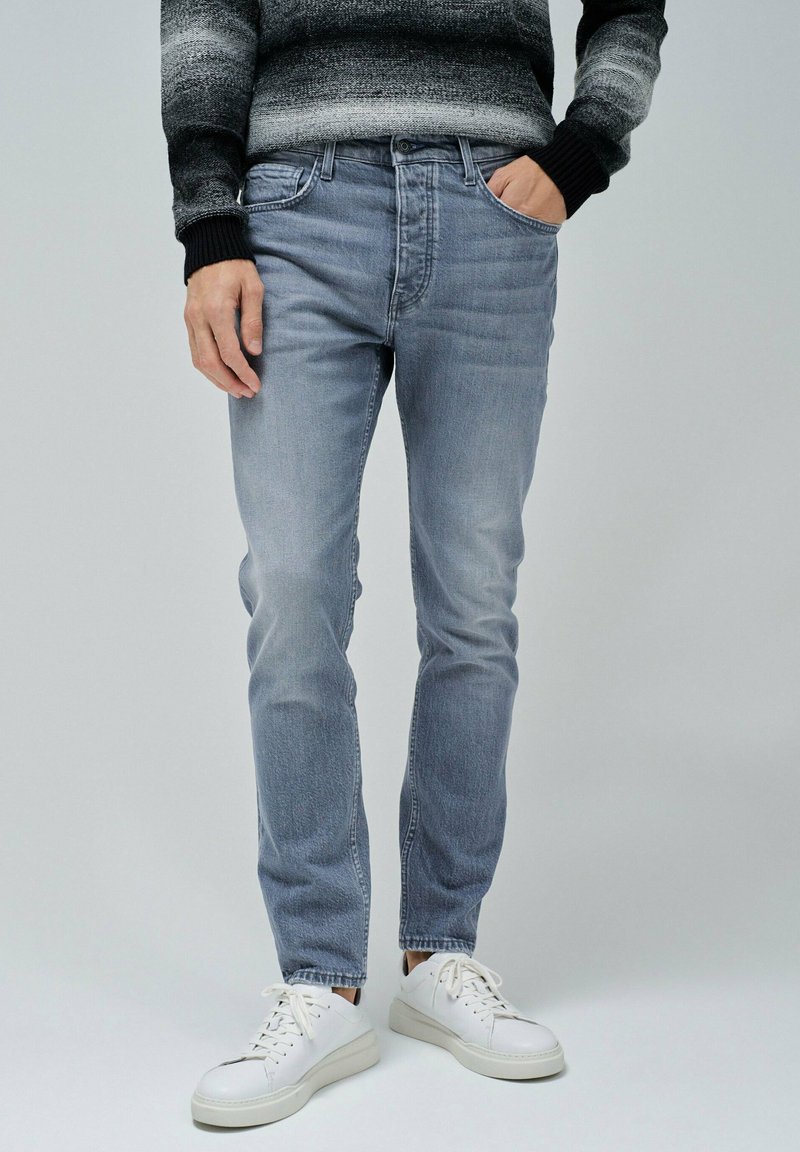 Jeans de mezclilla de color azul claro, con un corte ajustado, diseño de cinco bolsillos y un ligero desgaste, combinados con zapatillas blancas.