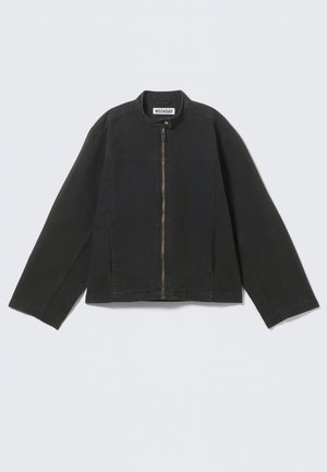 Veste noire à fermeture éclair avec manches longues, col montant et fermeture par bouton-pression au niveau du cou, posée à plat sur un fond clair.