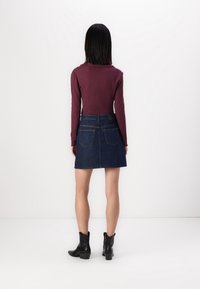 Gonna mini in denim scuro con vita aderente e due tasche posteriori, abbinata a un top a maniche lunghe a coste color bordeaux e stivaletti neri alla caviglia.