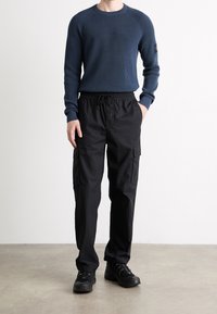 Granatowy sweter dzianinowy z teksturowanym wzorem, zestawiony z czarnymi spodniami cargo z bocznymi kieszeniami. Czarnym butom towarzyszy całość.