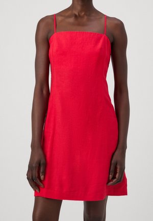 Czerwona mini sukienka bez rękawów z cienkimi ramiączkami, noszona przez osobę stojącą na gładkim tle.