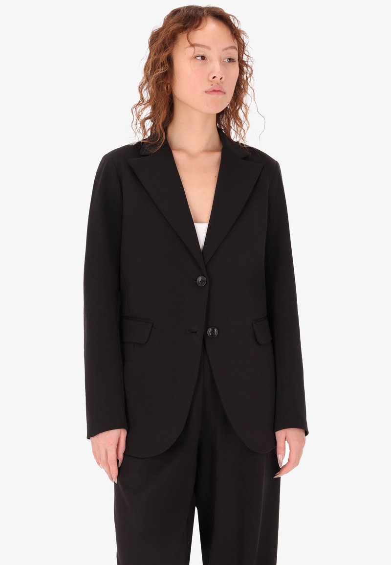 Blazer nero realizzato in tessuto testurizzato, con revers a punta, chiusura a due bottoni e tasche frontali. Vestibilità aderente con maniche lunghe.