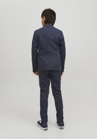 Traje azul marino con blazer de un solo botón y pantalones a juego. Tela texturizada, corte entallado, combinado con zapatillas casuales azul marino.