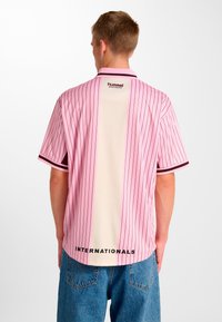 Lyserød stribet sportstrøje med cremefarvet ryg, med krave og sorte detaljer. Tekst "INTERNATIONALS" nederst. Casual pasform og korte ærmer.