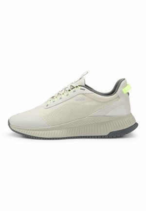 Chaussure de sport beige clair avec une tige texturée, des accents gris, des lacets réfléchissants et une semelle épaisse à rainures. Dispose d'une languette arrière pour un enfilage facile.