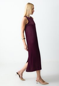 Robe sans manches bordée de bordeaux avec des fentes latérales, faite d'un tissu doux. Associée à des escarpins nude à bout pointu et à un bracelet en or au bras.