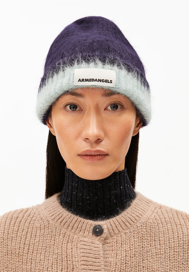 Lila und hellblaue Strickmütze mit flauschiger Textur und einem weißen Label mit der Aufschrift "ARMEDANGELS." Getragen über einem dunklen, gerippten Pulloverkragen.