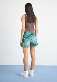 Un top maro fără mâneci asociat cu pantaloni scurți verzi cu un tipar geometric. Adidașii albi, în stil înalt, completează ținuta.