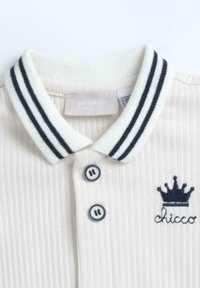 Polo blanc côtelé avec col rayé marine, doté de deux boutons marins et d'un logo couronne avec "chicco" brodé en marine.