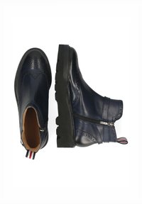 Botas de cuero azul marino hasta el tobillo con detalles de brogue, cierre de cremallera y una suela negra gruesa que cuenta con una tira a rayas en la parte posterior.