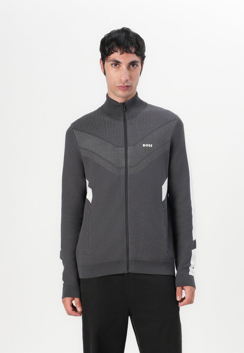 Dunkelgrau zip-up Jacke mit hohem Kragen, die mit strukturierten Mustern und weißen seitlichen Akzenten ausgestattet ist. Hergestellt aus weichem, dehnbarem Stoff.
