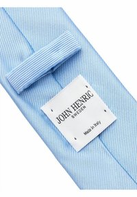 Vaaleansininen raidallinen kangas, jossa on sileä pinta, ja johon on kiinnitetty taitteeseen valkoinen etiketti, jossa lukee "John Henric Sweden Made in Italy".